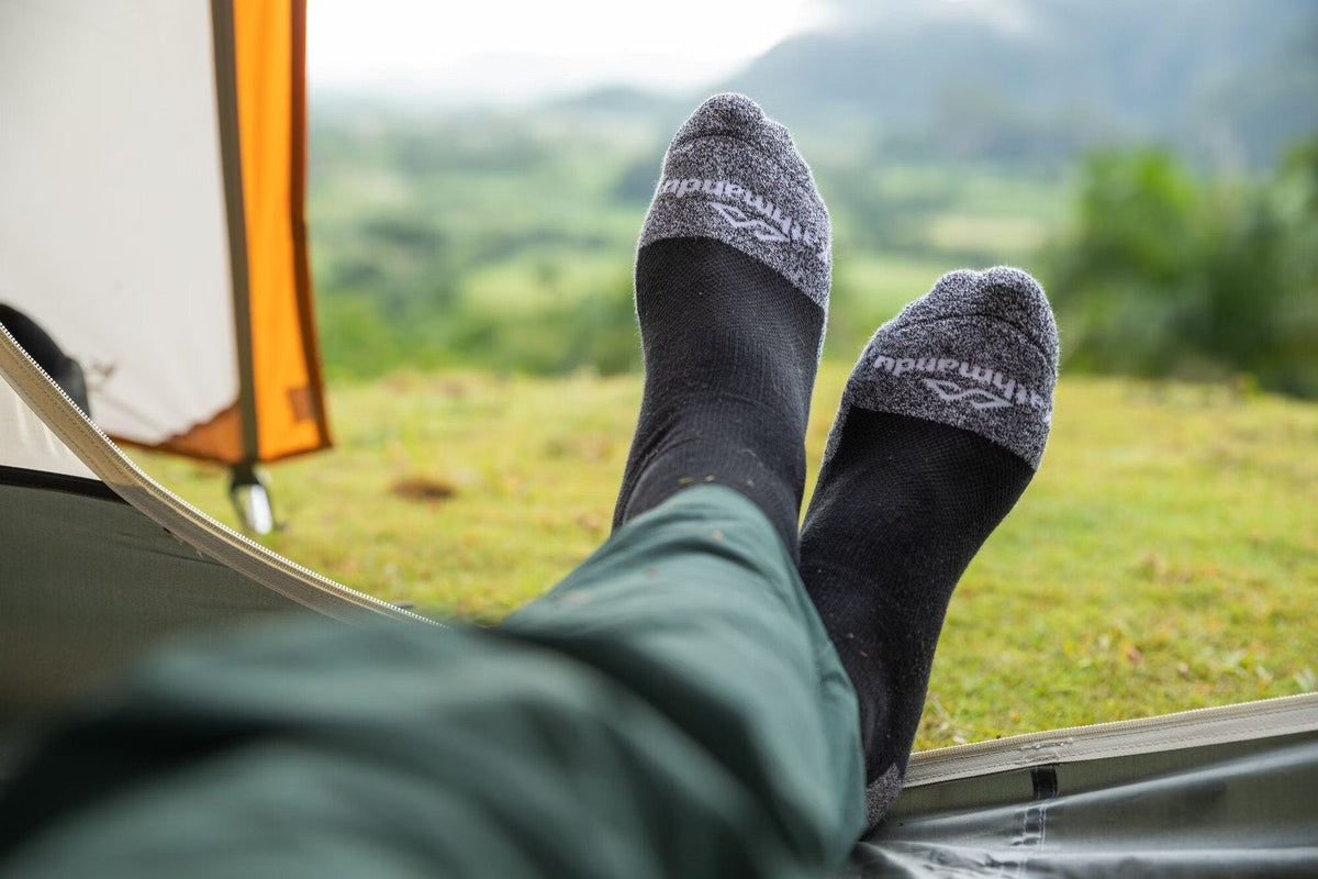 A camper is having a rest in his tent lying down with his feet at the edge of the tent.