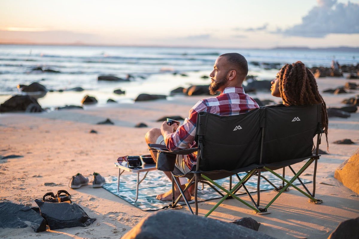 A couple is enjoying a sunset picnic on the beach.