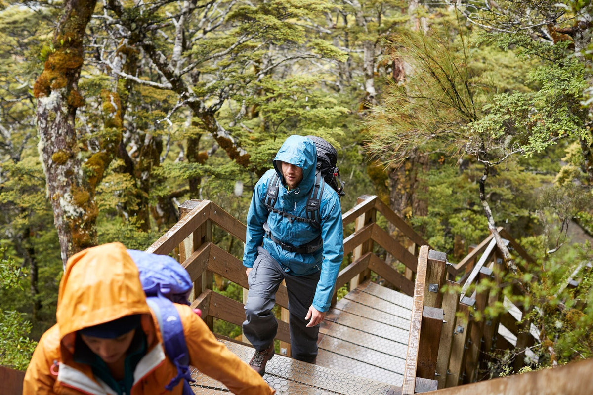 Two hikers walking up a wooden staircase on a trail in rain jackets